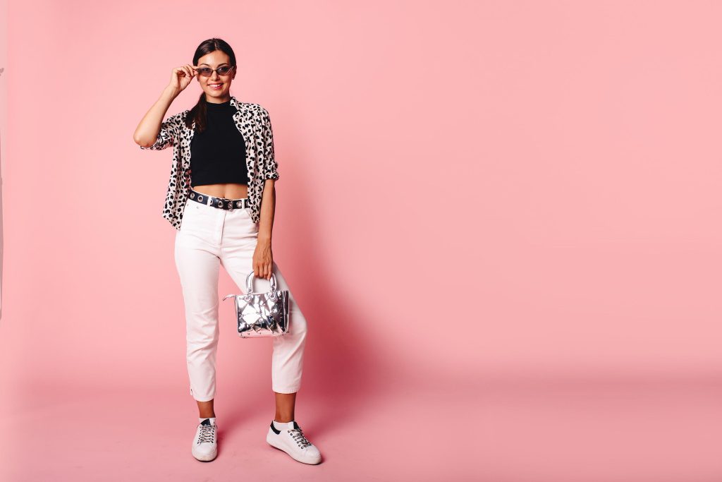 Mulher estilosa usando camisa animal print e calça branca em cenário rosa, representando estampa na moda atual