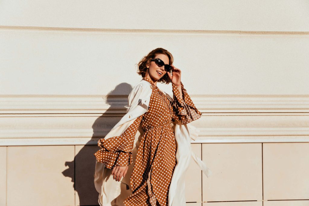 Mulher sorridente com vestido de poá marrom e branco, em estilo retrô moderno com movimento fluido