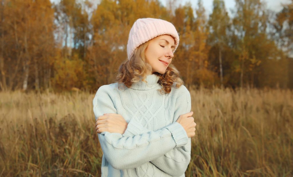 Mulher de suéter azul e gorro rosa em ambiente de outono frio, representando a paleta de inverno com tons suaves.