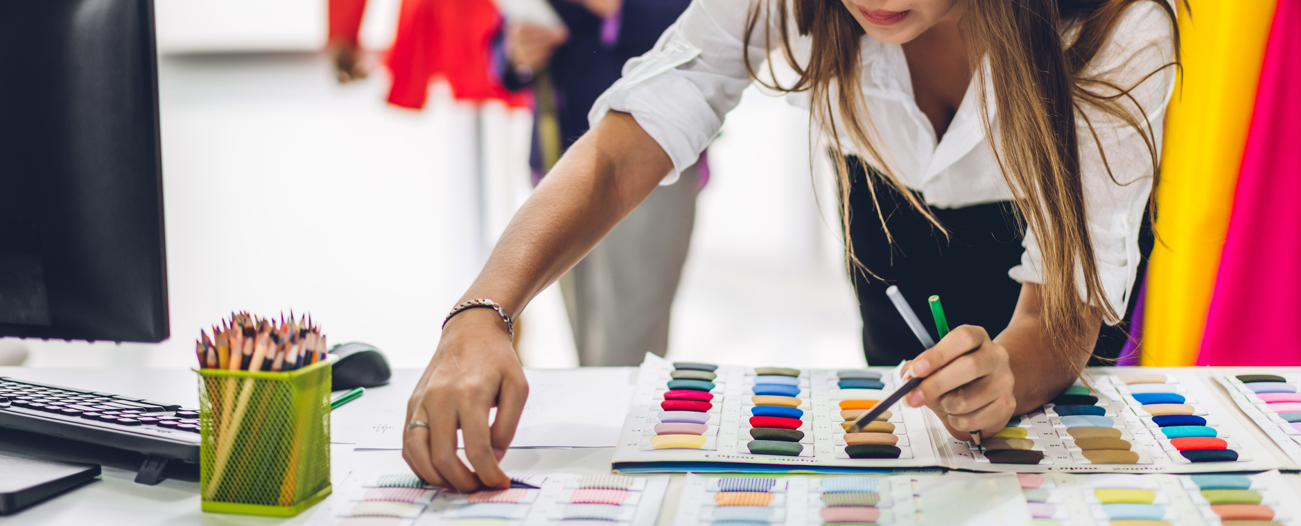 Designer de moda analisando cartela de cores e amostras têxteis no desenvolvimento de coleção.